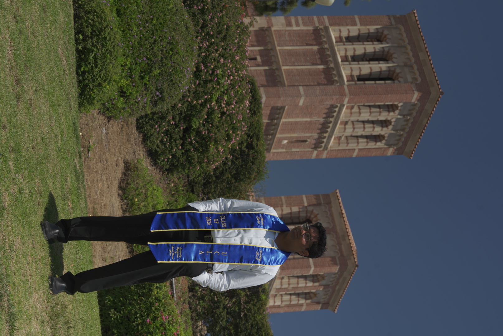 UCLA graduate standing on campus between the towers in a blue stole.